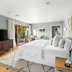 Bedroom with large bed, sliding glass doors to deck, TV on dresser, and chair with table at Hillside Hideaway in Topanga Canyon by Open Air Homes.