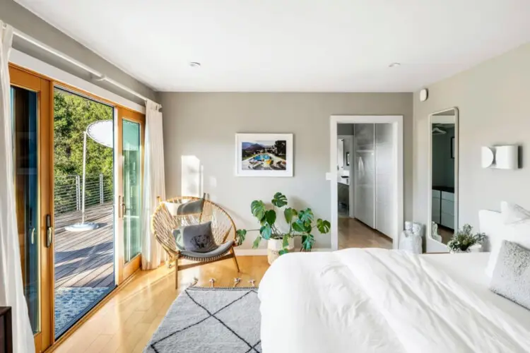 Bedroom with large bed, sliding glass doors to deck, and chair with table at Hillside Hideaway in Topanga Canyon by Open Air Homes.