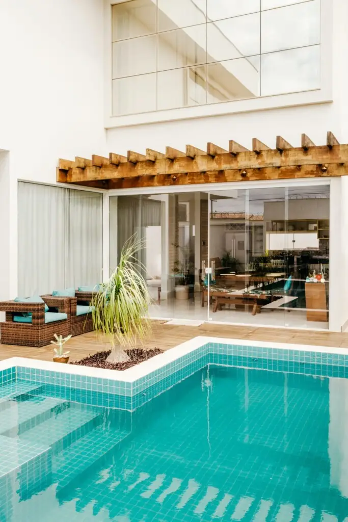 Modern house with a pool in the foreground, featuring a stylish outdoor seating area and large glass windows, likely part of a luxury vacation rental property.