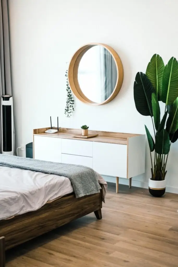 Modern bedroom with a wooden bed, a white dresser, and a large plant, likely part of a vacation rental property.