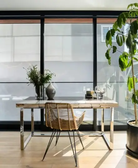 Desk with a chair in a room with large windows and plants.