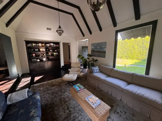 Living room with vaulted ceiling, striped sofa, and bookshelf at Beverly Grove Tudor Family Home - by Open Air Homes.