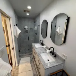 Bathroom with double vanity, two mirrors, and glass-enclosed shower at Beverly Grove Tudor Family Home - by Open Air Homes.