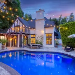 Evening view of Laurel Canyon Classic Hollywood Residence W/ Pool with illuminated stone patio, lounge chairs, umbrellas, and swimming pool by Open Air Homes.