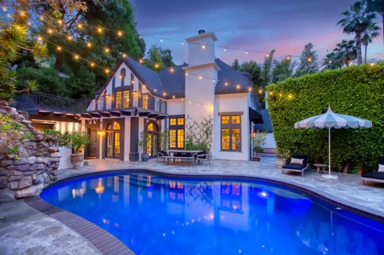 Evening view of Laurel Canyon Classic Hollywood Residence W/ Pool with illuminated stone patio, lounge chairs, umbrellas, and swimming pool by Open Air Homes.