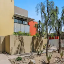 Exterior of a modern building with landscaped walkway and palm trees at La Mirage gated community in Palm Springs – by Open Air Homes.