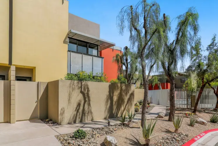 Exterior of a modern building with landscaped walkway and palm trees at La Mirage gated community in Palm Springs – by Open Air Homes.