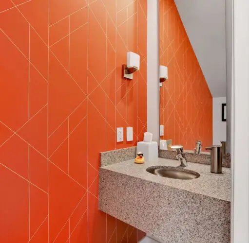 Bathroom with orange wall, sink, and mirror at La Mirage gated community in Palm Springs, featuring a vibrant and modern design – by Open Air Homes.