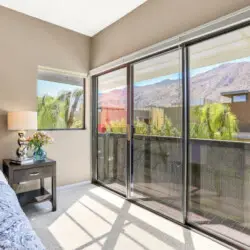 Bedroom with bed, side table, lamp, and sliding glass doors leading to a balcony with mountain view at La Mirage gated community in Palm Springs – by Open Air Homes.