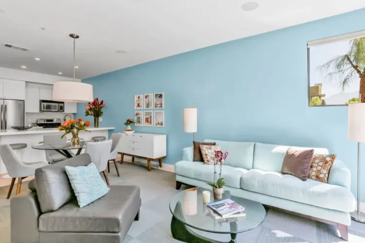 Living area with blue accent wall, sofa, chairs, and coffee table at La Mirage gated community in Palm Springs, featuring modern design – by Open Air Homes.