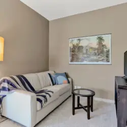 Living room with sofa, floor lamp, side table, and TV at La Mirage gated community in Palm Springs, providing a cozy and inviting space – by Open Air Homes.