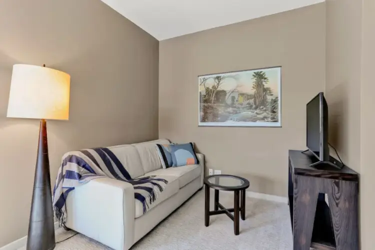 Living room with sofa, floor lamp, side table, and TV at La Mirage gated community in Palm Springs, providing a cozy and inviting space – by Open Air Homes.