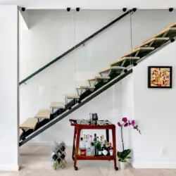 Modern staircase with glass railing and bar cart underneath at La Mirage - by Open Air Homes