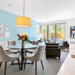 Dining area with glass table and pendant light, living area with fireplace and sliding glass door at La Mirage gated community in Palm Springs – by Open Air Homes.