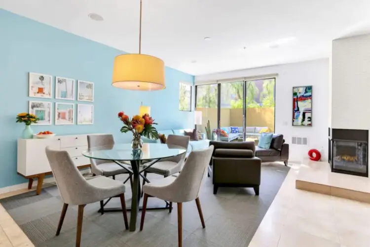 Dining area with glass table and pendant light, living area with fireplace and sliding glass door at La Mirage gated community in Palm Springs – by Open Air Homes.