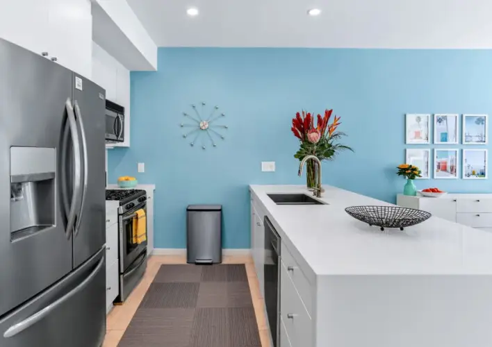 Kitchen with blue accent wall, white island, and stainless steel appliances at La Mirage gated community in Palm Springs, showcasing modern design – by Open Air Homes.