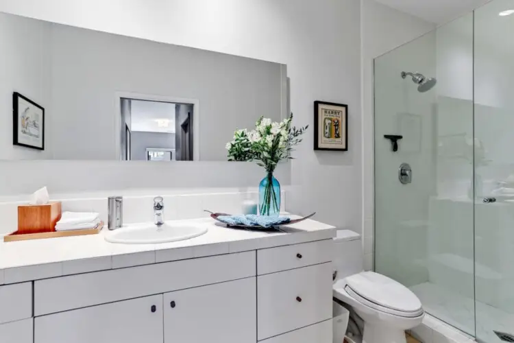 Bathroom with sink, mirror, and glass-enclosed shower at La Mirage gated community in Palm Springs, showcasing modern design – by Open Air Homes.