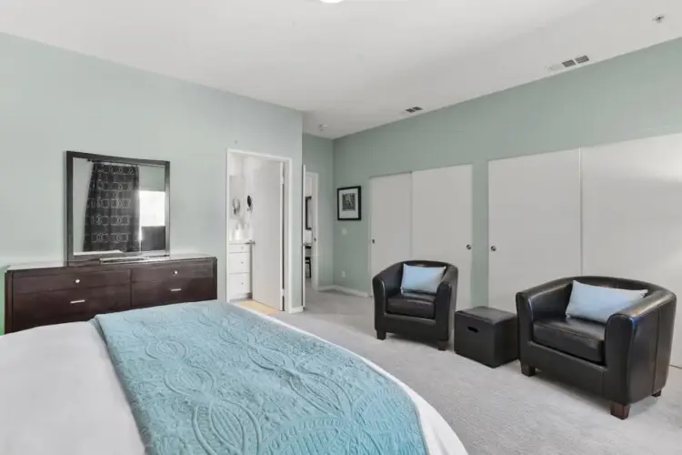 Bedroom with bed, two armchairs, and dresser at La Mirage gated community in Palm Springs, offering a comfortable and inviting space – by Open Air Homes.