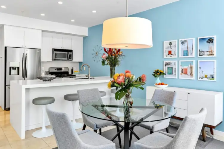 Modern kitchen and dining area with blue accent wall, white island, and dining table at La Mirage gated community in Palm Springs – by Open Air Homes.