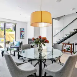 Dining area with glass table, chairs, and large pendant light at La Mirage gated community in Palm Springs, featuring modern design – by Open Air Homes.