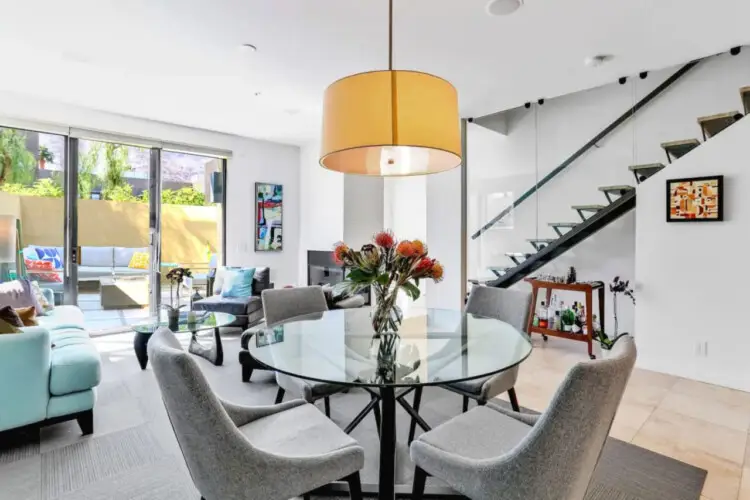 Dining area with glass table, chairs, and large pendant light at La Mirage gated community in Palm Springs, featuring modern design – by Open Air Homes.