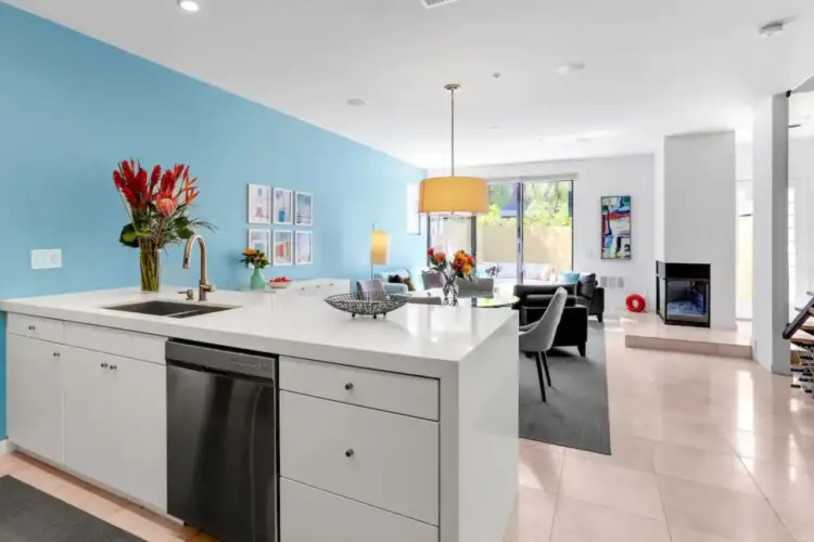 Kitchen with blue accent wall, white island, and dining area at La Mirage gated community in Palm Springs, featuring modern design – by Open Air Homes.