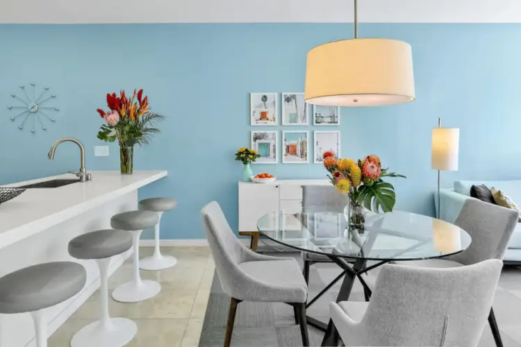 Dining area with blue accent wall, white island, and table with chairs at La Mirage gated community in Palm Springs, featuring a modern design – by Open Air Homes.