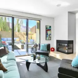 Living area with sofa, chairs, coffee table, fireplace, and sliding glass door leading to outdoor space at La Mirage - by Open Air Homes