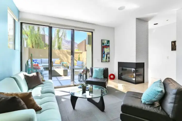 Living area with sofa, chairs, coffee table, fireplace, and sliding glass door leading to outdoor space at La Mirage - by Open Air Homes