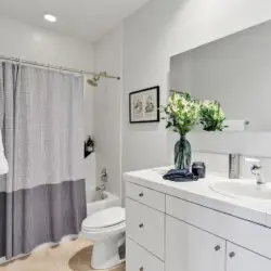 Bathroom with bathtub, shower curtain, sink, and vanity at La Mirage gated community in Palm Springs, showcasing clean and modern design – by Open Air Homes.