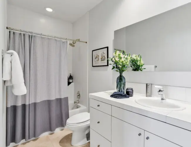 Bathroom with bathtub, shower curtain, sink, and vanity at La Mirage gated community in Palm Springs, showcasing clean and modern design – by Open Air Homes.