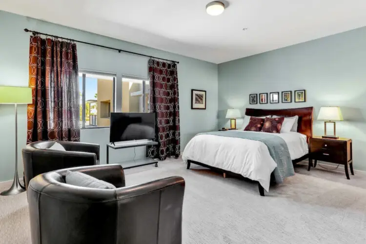 Bedroom with bed, armchairs, floor lamp, and TV at La Mirage gated community in Palm Springs, offering a comfortable and inviting space – by Open Air Homes.