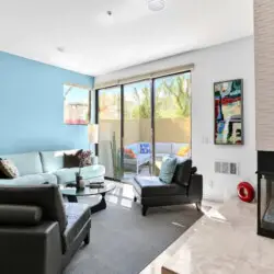 Living area with blue accent wall, fireplace, and sliding glass door at La Mirage gated community in Palm Springs, offering a modern design – by Open Air Homes.