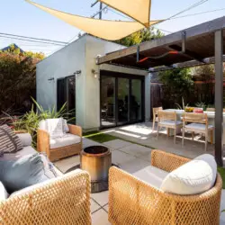 Outdoor seating area with sofas, chairs, and a table under a shaded canopy at Sun-Drenched Spanish Manor in Mar Vista - by Open Air Homes.