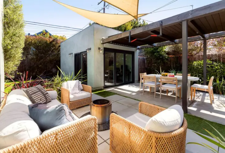 Outdoor seating area with sofas, chairs, and a table under a shaded canopy at Sun-Drenched Spanish Manor in Mar Vista - by Open Air Homes.