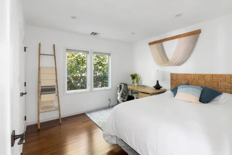 Bedroom with bed, bedside table, and window with tree view at Sun-Drenched Spanish Manor in Mar Vista - by Open Air Homes.