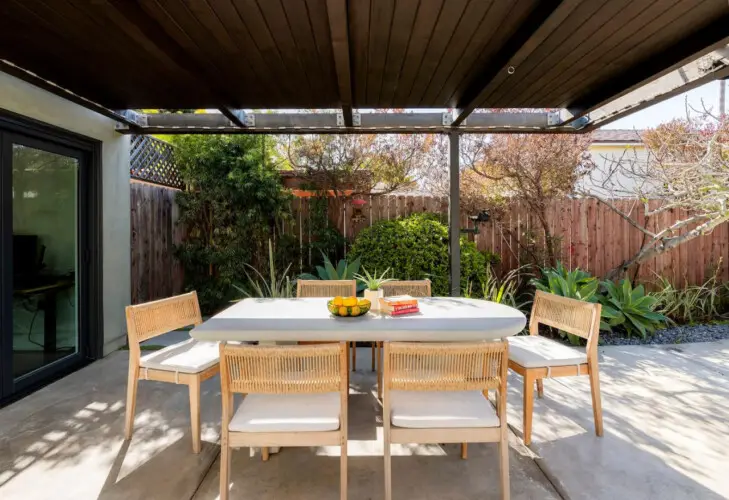 Outdoor dining area with table and chairs under a pergola at Sun-Drenched Spanish Manor in Mar Vista - by Open Air Homes.