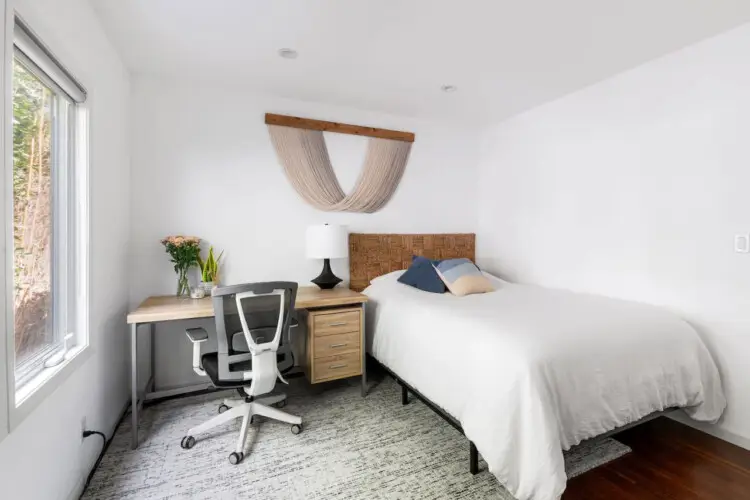 Bedroom with bed, bedside table, window, and desk with chair at Sun-Drenched Spanish Manor in Mar Vista - by Open Air Homes.