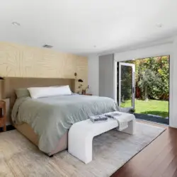 Bedroom with bed, wooden dresser, mirror, and potted plant at Sun-Drenched Spanish Manor in Mar Vista - by Open Air Homes.