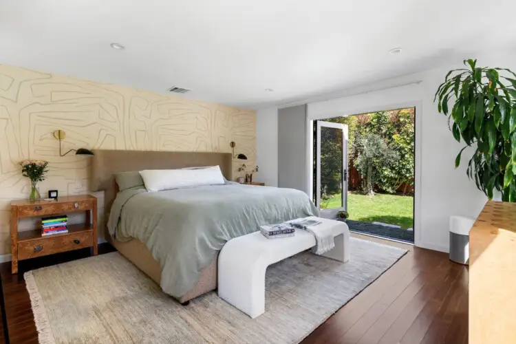 Bedroom with bed, wooden dresser, mirror, and potted plant at Sun-Drenched Spanish Manor in Mar Vista - by Open Air Homes.