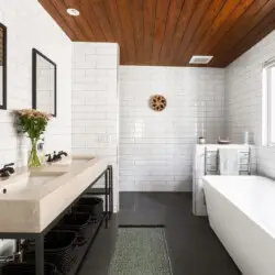 Bathroom with large bathtub, white tiles, and wooden ceiling with skylight at Sun-Drenched Spanish Manor in Mar Vista - by Open Air Homes.