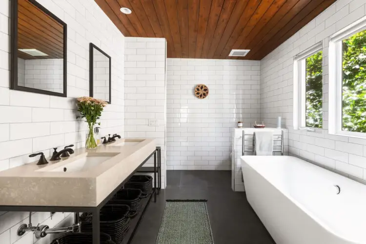 Bathroom with large bathtub, white tiles, and wooden ceiling with skylight at Sun-Drenched Spanish Manor in Mar Vista - by Open Air Homes.