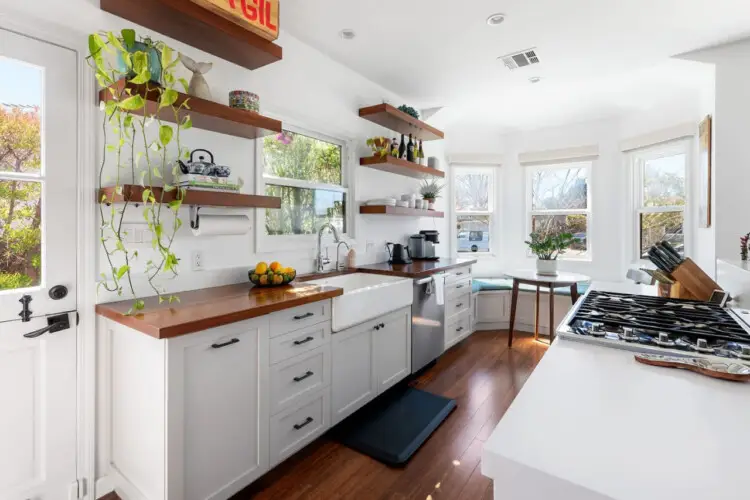 Bright kitchen with white cabinets, wooden countertops, and open shelving at Sun-Drenched Spanish Manor in Mar Vista - by Open Air Homes.