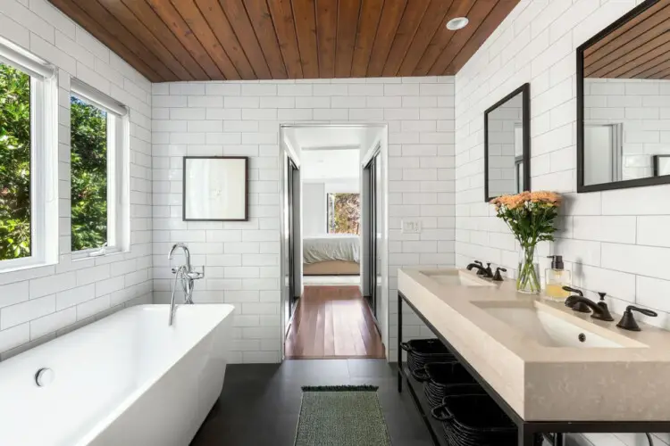 Bathroom with large bathtub, white tiles, and wooden ceiling at Sun-Drenched Spanish Manor in Mar Vista - by Open Air Homes.