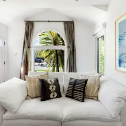 Living room with white sofa, decorative pillows, and large window at Sun-Drenched Spanish Manor in Mar Vista - by Open Air Homes.