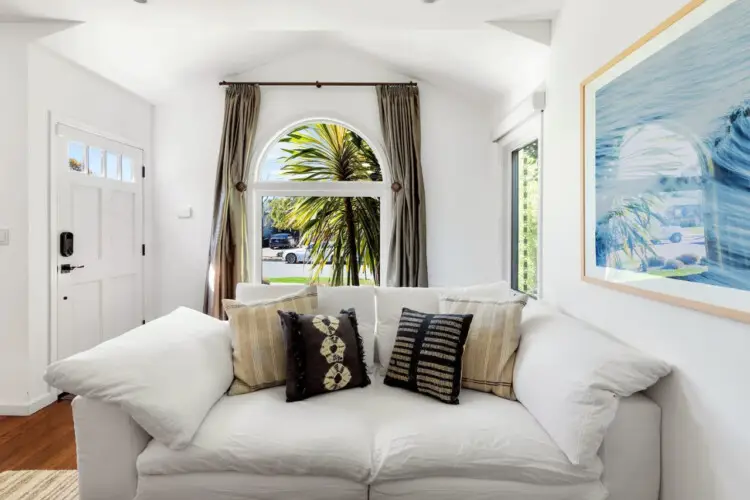 Living room with white sofa, decorative pillows, and large window at Sun-Drenched Spanish Manor in Mar Vista - by Open Air Homes.