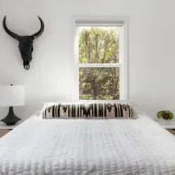 Bedroom with bed, bedside table, lamp, and window at Sun-Drenched Spanish Manor in Mar Vista - by Open Air Homes.