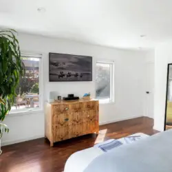 Bedroom with bed, wooden dresser, mirror, and potted plant at Sun-Drenched Spanish Manor in Mar Vista - by Open Air Homes.