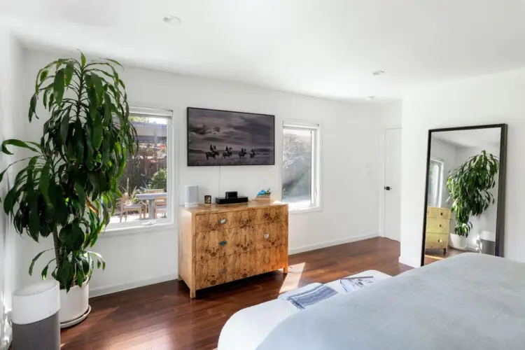 Bedroom with bed, wooden dresser, mirror, and potted plant at Sun-Drenched Spanish Manor in Mar Vista - by Open Air Homes.