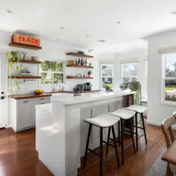 Kitchen with white island, bar stools, and open shelving at Sun-Drenched Spanish Manor in Mar Vista - by Open Air Homes.